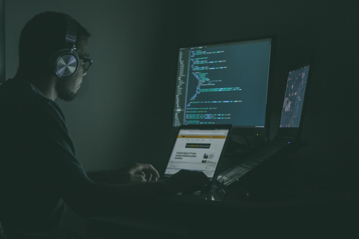 A developer working at a laptop in front of monitors showing code